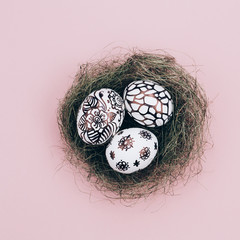 Three easter eggs are painted in black and white lie in a green nest. 