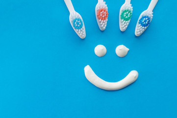 Multicolored toothbrushes on a blue background with a smile painted with toothpaste. The view from the top.