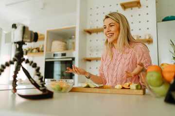 Young food blogger with beautiful smile is recording new video recipe. Young woman is preparing fruit salad at home.