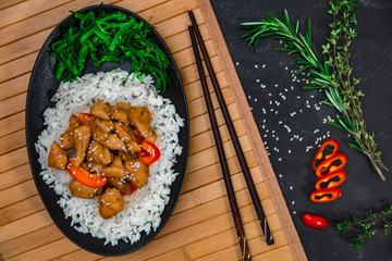 Chinese dish on stone background. Chicken with rice in black plate on wooden board. Horizontal shot.