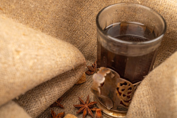 A faceted glass of tea in a vintage Cup holder and a star anise on a background of rough homespun fabric. Close up.