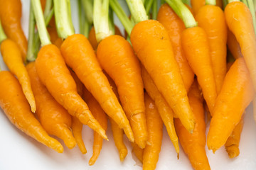 Pile of fresh raw baby carrots with green leaves isolated on white background, vegetable food concept