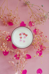 Glass with milk on a pink background with heart shaped confetti