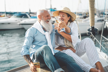 Senior couple toasting champagne on sailboat vacation - Happy elderly people having fun celebrating...