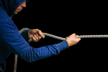 Hands with a rope on a black background. A man pulls a rope wrestling. Drag the business to your side.