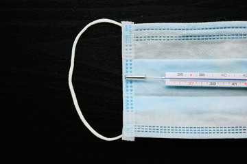Top view of medical protective mask and thermometer on black background.