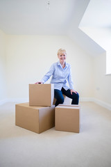 Portrait Of Senior Woman Downsizing In Retirement Sitting On Boxes In New Home On Moving Day