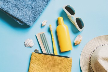 Summer beach essentials. Blue cotton towel, yellow cosmetic bag, wooden comb, toothbrush, sunscreen...