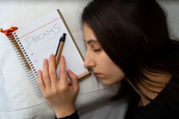 Notebook with the word Dreams written, next to a sleeping woman.