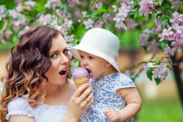 Young beautiful mom with daughter in hat eating ice cream in park in spring