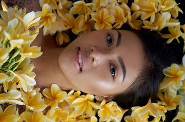 Obraz na płótnie Canvas Asian girl portrait face in yellow plumeria frangipani flowers. Beautiful Balinese women. Beauty salon and massage spa concept