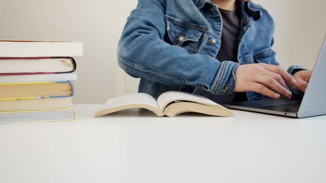 Young millennial using a laptop to write information from the book, studying home concept
