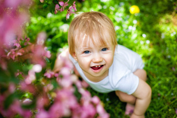 Close-up portrait of a 1-2 year old girl outdoors in a garden with pink flowers in the trees.