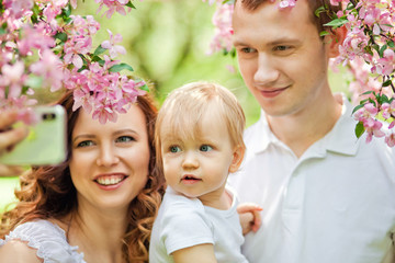 Happy family in the spring garden. Mother father and little daughter together in a blooming Sakura Park.