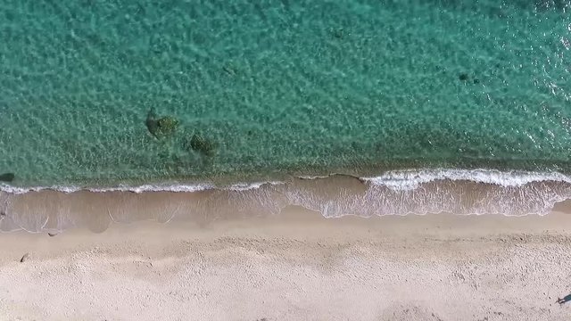 aerial view of a beach shoreline with crystal clear water, waves and white sand 