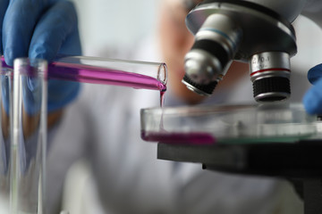 Close-up of lab assistant hand holding test-tube. Scientist adding reagent in container. Chemist examining chemical reaction of sample. Scientific experiments concept