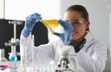 Close-up of researcher holding beaker with yellow liquor. Smiling scientist looking at test tube with gladness. Chemistry industry and investigation concept
