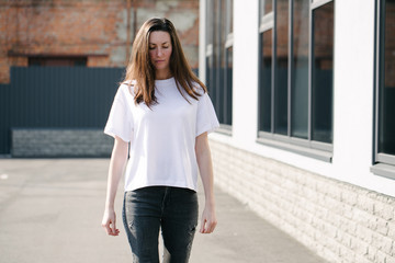 Skinny woman wearing white blank t-shirt and black jeans with space for your logo or design in casual urban style over city street background