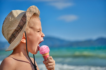 White blond boy with hat at seaside eating or licking ice cream with shallow depth of field and copyspace