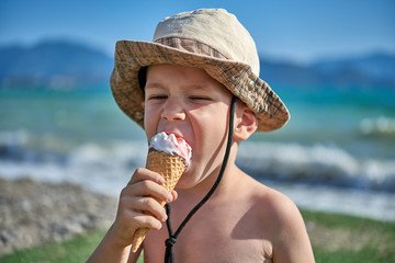 Ice cream licking / eating boy with hat on seaside / beach with shallow depth of field.