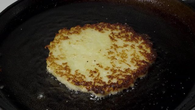 Potato pancakes draniki are fried in vegetable oil in a pan, macro shot