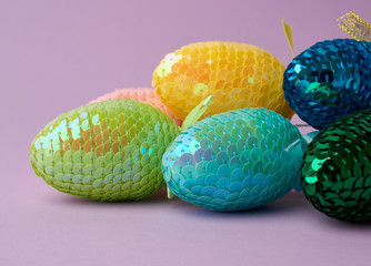 multicolored decorative Easter eggs decorated with sequins on a purple background