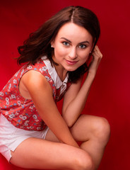 Portrait of a stunning sexy young brunette girl on a red background, a floral print blouse and white short shorts. Beauty and Fashion