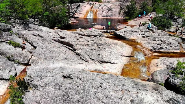 Aerial shot of tourists swimming, relaxing and arriving at Conceicao dos Gatos Waterfall, Chapada Diamantina, Bahia, Brazil. Drone moving Backward
