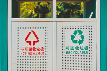 Trashcan in park. Trashcan in park. Iron tank with chineese and english words recyclable and not-recyclable, for the processing of debris is in the alley. Close-up.
