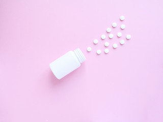 scattered vitamin pills from bottle on pink background. Space for design, flat lay. Concept boost immune system, medicine and tablets.