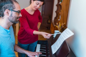 Piano lessons at home concept. Female teacher explaining a music class to middle age man student....