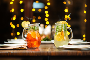Two fresh fruit lemonade in jugs on a laid table, restaurant, horizontal, side view
