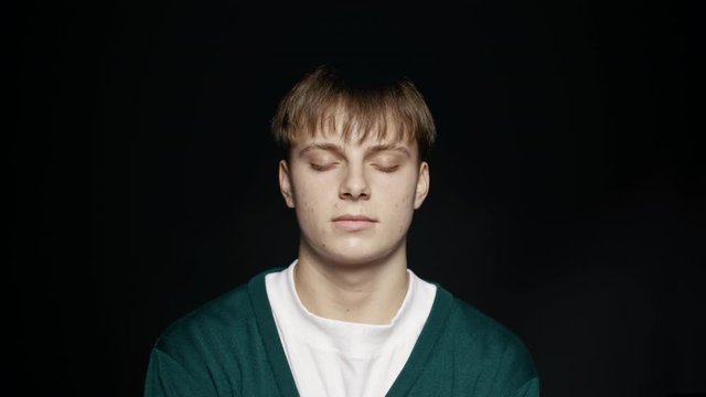 Close up of young man with his eyes closed against black background. Young man standing with closed eyes.
