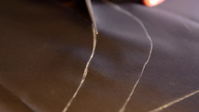 A tailor is cutting lines on a acetate silk lining fabric with his chalk in order to make a suit