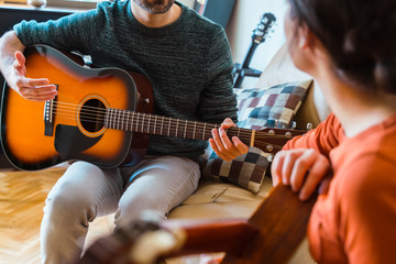 Unrecognizable guitar teacher explaining a music class to female student. Woman learning an instrument at home. Music course online concept. Indoor leisure lifestyle for young people.