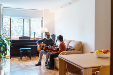Panoramic view of woman receiving musical course in her house. Leisure and artistic hobby indoors. Indoor music class at home. Teacher explaining guitar lessons to young female student.