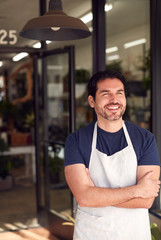 Smiling Male Owner Of Florists Standing In Doorway Surrounded By Plants