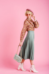 Full-length studio fashion portrait of young elegant happy smiling woman wearing trendy spring outfit: floral print blouse, green pleated skirt, white ankle boots, holding stylish  faux leather bag - obrazy, fototapety, plakaty
