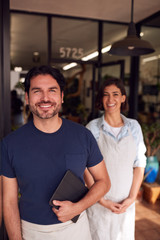 Portrait Of Male And Female Owners Of Florists With Digital Tablet Standing In Doorway With Plants