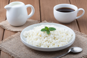 Cottage cheese in a  plate, coffee and milk on a wooden table