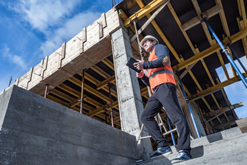 An architect at a construction site looks into the distance. A man in construction clothing. Man with tablet near construction site. Cogncept - builder is waiting for building materials