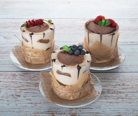 tiramisu in a glass with berries, mint and coffee beans on a light wooden background
