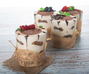 tiramisu in a glass with berries, mint and coffee beans on a light wooden background