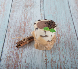 tiramisu in a glass with berries, mint and coffee beans on a light wooden background