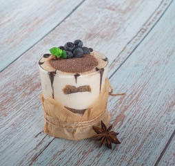 tiramisu in a glass with berries, mint and coffee beans on a light wooden background