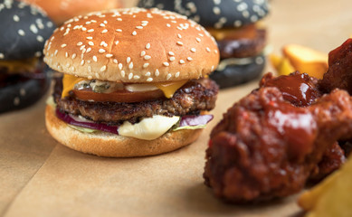 hamburgers with yellow and black rolls on parchment paper with breaded chicken wings and French fries