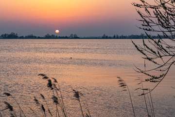 The setting sun almost disappears behind the shore of Lake Zoetermeerse Plas in Zoetermeer, The...