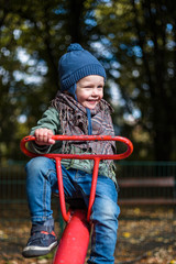 Little cheerful boy in a blue cap on a red seesaw