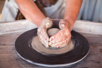 Potter's wheel with clay. Women's hands make a vase of clay.