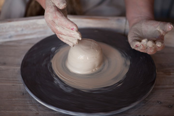 Potter's wheel with clay. Women's hands make a vase of clay.